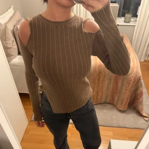 Brun ribbad tröja med cut-out detaljer - Säljer en snygg brun ribbad tröja med unika cut-out detaljer vid axlarna. Tröjan har långa ärmar och en snörning på sidan som ger en cool look. Perfekt för att ge din outfit det lilla extra! Aldrig använd, i super bra skick!🤍