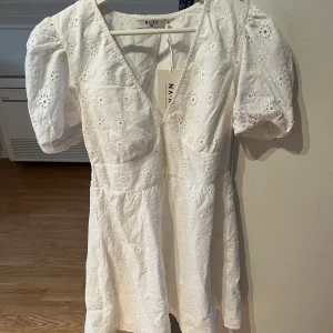 Vit klänning med puffärm från NA-KD - Säljer en söt vit klänning från NA-KD med puffärmar och v-ringning. Passar perfekt till studenten. Klänningen har ett broderat mönster av blommor. Den är i storlek EU 34 och är helt oanvänd, endast prövad. Lappen finns kvar på.