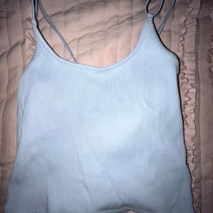 Ljusblå ribbad linnetopp från 157 - Säljer en ljusblå ribbad linnetopp från 157 med tunna axelband. Perfekt för varma dagar och enkel att matcha med andra plagg. Toppen har en stilren design och är tillverkad i ett mjukt material.