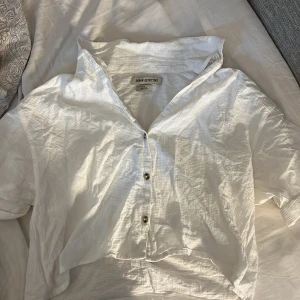 Vit kortärmad skjorta från Urban Outfitters - Säljer en stilren vit skjorta från Urban Outfitters. Skjortan har korta ärmar och knappar. Testade bara på snabbt så ser lite konstigt ut att ha svart linne under men den är jättefin till ex jenas kjol på sommaren! Köpte i Paris o har aldrig använt