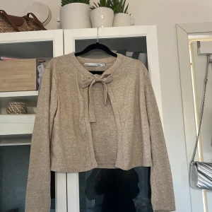 Beige kofta från 157 - Säljer en stilren beige kofta från 157 i storlek XS. Koftan har långa ärmar och en söt knytning framtill. Perfekt för lager-på-lager under kyligare dagar. Passar till både jeans och kjol för en avslappnad look. Skriv privat för fler bilder🌸