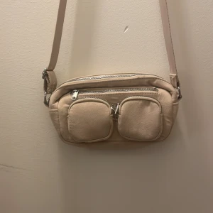 Beige axelväska med dragkedja - Snygg beige axelväska med flera praktiska fack och dragkedjor. Perfekt för att hålla ordning på dina saker. Väskan har en justerbar axelrem och är tillverkad i ett mjukt material.