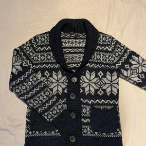 Mönstrad kofta med knappar - Säljer en mysig kofta med ett vackert mönster i vitt och mörkblått. Koftan har långa ärmar och stora knappar framtill. Perfekt för kyliga dagar!