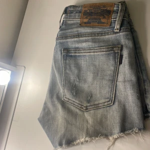 Jeansshorts från Crocker - Snygga ljusblå jeansshorts från Crocker med slitna detaljer och fransig kant. Perfekta för en avslappnad stil. De har en klassisk femficksdesign och knappgylf.