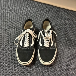 Svarta och vita sneakers från Vans - Säljer ett par klassiska svarta och vita Vans sneakers med snörning. Skorna har en vit sula och den ikoniska sidostripen i vitt. Perfekta för en avslappnad stil.