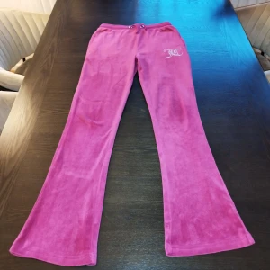 Rosa mjukisbyxor från Juicy Couture - Snygga rosa mjukisbyxor från Juicy Couture med glittrande logga på höften. Byxorna har en bekväm passform och dragsko i midjan för justerbarhet. Perfekta för en avslappnad stil med en touch av glamour. Priset kan diskuteras!! Nypris: 1100 kr