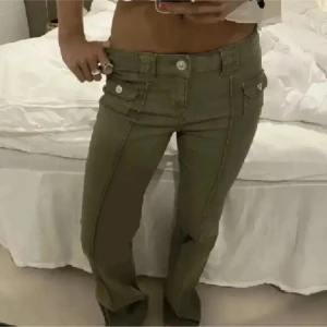 Olivgröna byxor med knappar💕 - Snygga olivgröna byxor med låg midja och bootcut-stil. Byxorna har dekorativa knappar och fickor framtill, vilket ger en cool och avslappnad look. Perfekta för en trendig vardagsstil.