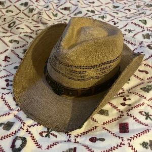 Beige cowboyhatt med bälte - Snygg beige cowboyhatt i flätat material med ett dekorativt bälte runt kullen. Perfekt för en avslappnad cowboy-look. Från SkoUno.