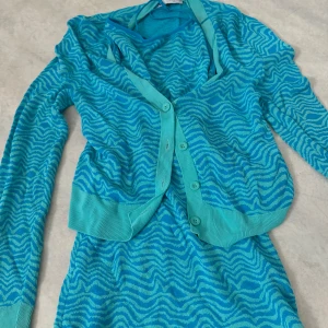 Turkos kofta med vågmönster - Säljer en snygg turkos kofta med ett vågigt mönster. Koftan har en v-ringad design och knappar framtill. 