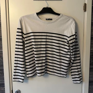 Randig tröja från Zara - Säljer en stilren vit och svart randig tröja från Zara. Tröjan har långa ärmar och en klassisk rund halsringning. 