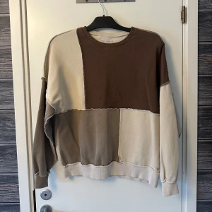 Beige och brun tröja från Pull&Bear - Säljer en cool tröja från Pull&Bear i beige och bruna toner. Tröjan har ett patchwork-mönster med långa ärmar och rund hals. 