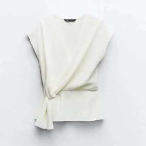 Vit omlottopp från Zara - Elegant vit omlottopp från Zara med knytning i sidan. Toppen har korta ärmar och en stilren design som passar perfekt för både vardag och fest. Inga defekter!! 💕💕har lagt den billigaste frakten🫶