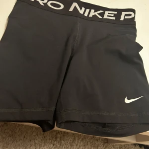 Svarta träningsshorts från Nike Pro - Säljer ett par svarta Nike Pro träningsshorts med Dri-FIT-teknologi. De har en elastisk midja med Nike-logga och är perfekta för intensiva träningspass. Shortsen är designade för att ge en tight passform och maximal rörelsefrihet.