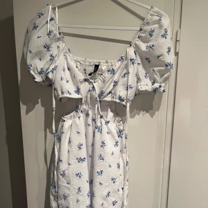Vit blommig klänning med puffärmar - Charmig vit klänning med blå blommor och puffiga kortärmar. Den har en söt knytning framtill och en smickrande passform. Perfekt till sommaren, endast använd en gång på midsommar!!☀️☀️