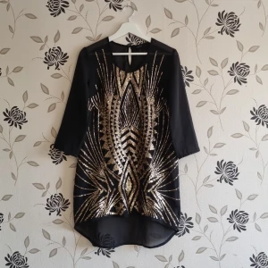 Svart tunn blus med guldpaljetter från Lindex, Strl: S - Snygg svart klänning från Lindex med glittrande guldpaljetter i ett geometriskt mönster. Klänningen har trekvartsärmar och en rund halsringning. Perfekt för en festlig kväll! Den är lite tråkigt på vissa ställen, se bilder.