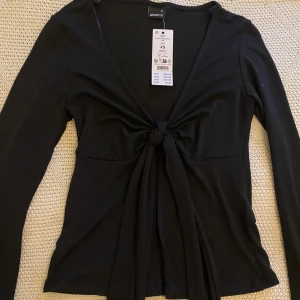 Svart långärmad topp från Gina Tricot💘💘 - Svart långärmad topp från Gina Tricot med knytning framtill💓köpte i somras men kom aldrig till användning och lappen är kvar💘säljer för halva priset och är Ny-sick. 