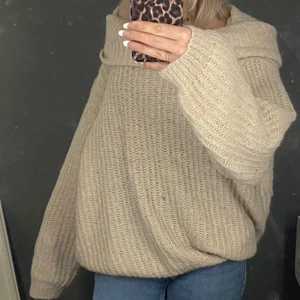 Beige stickad tröja - Mysig beige stickad tröja med en avslappnad passform. Perfekt för kyliga dagar med sin mjuka och bekväma design. Tröjan har långa ärmar och en bred krage som ger extra värme och stil.
