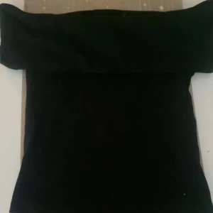 Svart offshoulder topp - Snygg svart offshoulder topp med en elegant design. Perfekt för en stilren look. Toppen har en tight passform och är tillverkad i ett mjukt material.