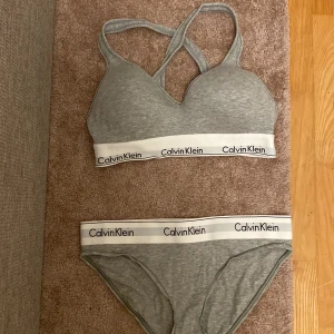 Grå bralette från Calvin Klein - Snyggt och bekvämt grått set med både trosor och bh från Calvin Klein. Bh-n har korsade axelband och både över och underdel har en vit kant med loggan. Sååååå snygga! Passar alla med storlek S! Köptes på Åhléns för ca 500 kr och jag säljer för 200! Bh-n är använd några fåtal gånger och trosorna är endast provade💕hör av er vid intresse eller om ni har frågor!