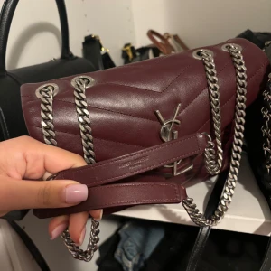 Vinröd väska från YSL - Lou Lou medium, köpt på collectors cage. Väl använd och saknar ena magneten till låset vilket gör att den inte går att stänga men det kan lagas. Annars i bra skick. Väskan är äkta och autentiserad hos collectors cage men kommer inte med något orginlakvitto, låda, dustbag, vilket också är anledningen till det låga priset. 