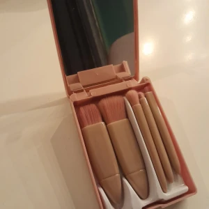 Set med sminkborstar i etui - Praktiskt set med sminkborstar i ett kompakt etui med spegel. Innehåller fem borstar med trähandtag och mjuka borst, perfekt för olika sminkapplikationer. Etuiet är i en ljusrosa färg och lätt att ta med sig.