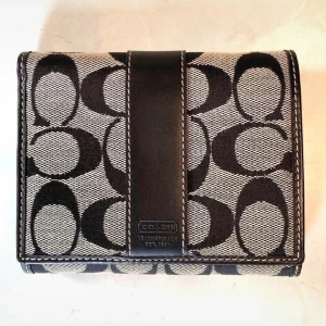 Coach Wallet  - Snygg plånbok från Coach i svart och beige med ett ikoniskt mönster. Tillverkad i en kombination av skinn och syntetmaterial. Perfekt för att hålla ordning på kort och kontanter.