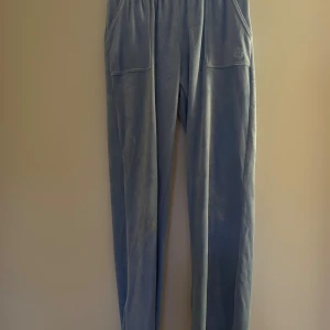 Blå juicy couture  - Säljer ett par bekväma blå Juicy Couture byxor  med två fickor bak som har knappar. Byxorna har en broderad logga på sidan och är perfekta för en avslappnad stil.  Stl. 10-11 år. Fint skick!