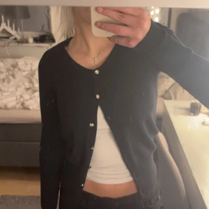 Svart kofta från Copenhagen Luxe - Snygg svart kofta från Copenhagen Luxe med glittriga knappar. Perfekt för att lägga till lite extra stil till din outfit. Koftan har en klassisk design med långa ärmar.