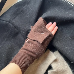 Bruna fingerlösa vantar - Säljer ett par bruna fingerlösa vantar med ribbstickade muddar. Perfekta för att hålla händerna varma samtidigt som du kan använda fingrarna fritt. De har en praktisk design och är lätta att matcha med olika outfits.