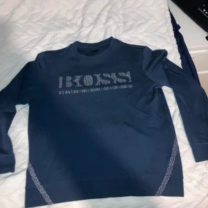 Mörkblå tröja från Hugo Boss - Säljer en stilren mörkblå tröja från Hugo Boss med ett iögonfallande BOSS-tryck på framsidan. Tröjan har långa ärmar och en rund halsringning. Perfekt för en avslappnad men ändå snygg look.