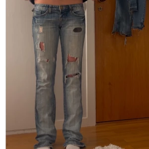 Blå slitna jeans - Säljer ett par coola blå jeans med slitningar och hål. De har en låg midja och är bootcut/straight. Jätte coola!