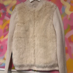 Vit stickad kofta med pälsdetaljer  - Säljer en stilren vit stickad kofta från Primark med mjuka pälsdetaljer på framsidan. Jackan har en hög krage och långa ärmar, perfekt för kyliga dagar. Den är både mysig och trendig, ett måste i garderoben!