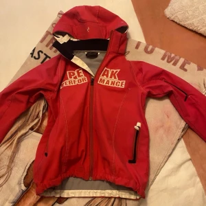 Röd jacka från Peak Performance stl 160 - Snygg röd jacka från Peak Performance med huva och dragkedja. Perfekt för aktiva dagar med stil. Jackan har praktiska fickor och detaljer i vitt.