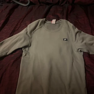 Grön tröja från Nike - Säljer en stilren gröna tröja från Nike med rund hals och en liten logotyp på bröstet. Tröjan har långa ärmar och en praktisk dragkedja på sidan. Perfekt för en avslappnad look.