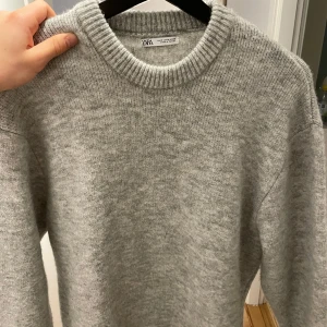 Grå stickad tröja från Zara - Säljer en stilren grå stickad tröja från Zara. Perfekt för kyligare dagar med sin mjuka och bekväma passform. Tröjan har långa ärmar och en klassisk rund halsringning. Tröjan är knappt använd och är därför i nyskick. Ordinarie pris 599kr 