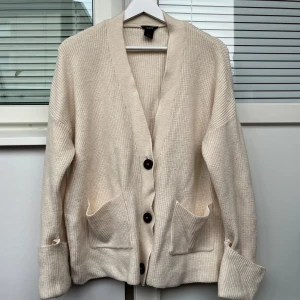 Beige kofta från Lindex - Mysig beige kofta från Lindex med stora knappar och praktiska fickor framtill. Perfekt för kyliga dagar med sin stickade design och långa ärmar. En klassisk och stilren look som passar till det mesta.