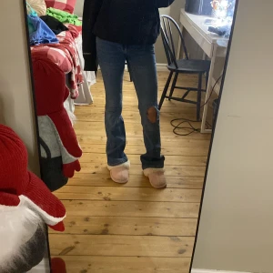 Blå jeans från Gina Tricot - Säljer ett par blå jeans från Gina Tricot med en snygg slitning på ena benet. De har en klassisk femficksdesign och knappar i midjan. Perfekta för en avslappnad stil.