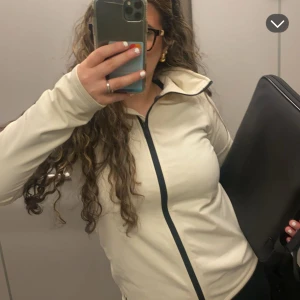 Beige långärmad tröja med dragkedja - Snygg beige långärmad tröja med dragkedja framtill. Perfekt för en avslappnad stil och enkel att matcha med andra plagg. Den har en stilren design med mörka detaljer längs dragkedjan.