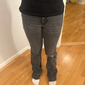Grå jeans med slitningar - Säljer ett par grå jeans med slitningar på knäna. De har en klassisk femficksdesign och en bekväm passform. Perfekta för en avslappnad stil.