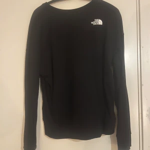 Svart tröja från The North Face - Säljer en svart tröja från The North Face med deras ikoniska logga i vitt på bröstet. Tröjan har långa ärmar och en klassisk passform, perfekt för vardagsbruk.