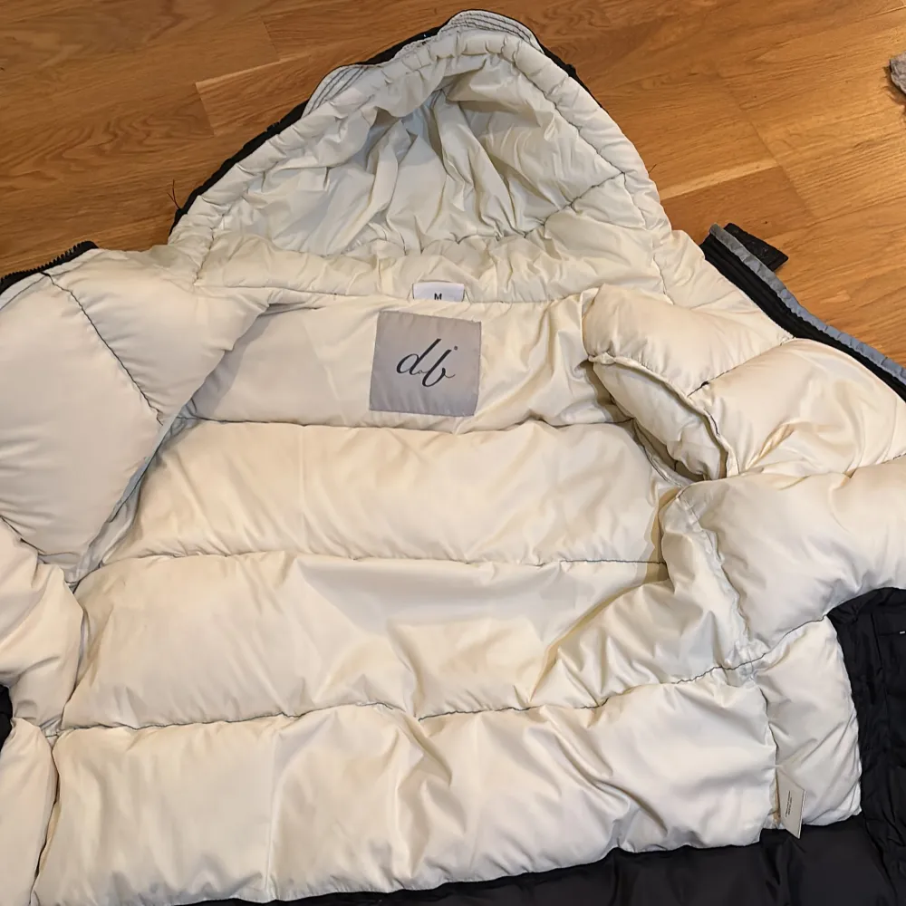 Snygg svart dunjacka/puffer från D.brand med en mysig vit insida. Jackan har en praktisk huva och dragkedja framtill. Märkesdetalj på ärmen ger en extra touch. Perfekt för kyliga dagar! Skick 9/10. Pris kan diskuteras. Passar som XS. Takit.