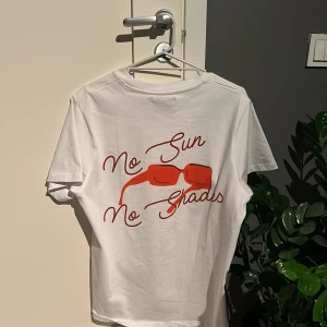 Vit t-shirt från pica pica - Vit t-shirt med ett coolt tryck av röda solglasögon och texten 'No Sun No Shades' på baksidan. Framsidan har en liten röd textdetalj med tröjans märke. Perfekt för en avslappnad stil.