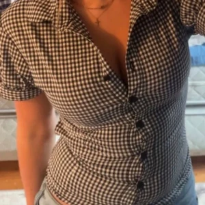 Svartvit rutig blus - Snygg svartvit rutig blus med korta ärmar och knappar framtill. Perfekt för en stilren look.