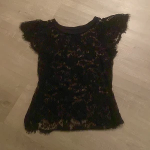 Svart spetsblus från Lindex - Snygg svart spetsblus från Lindex i storlek S. Blusen har korta ärmar och ett elegant spetsmönster som ger en stilren look. Perfekt för att klä upp en outfit.