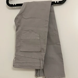 Grå byxor med dragkedja från River Island - Snygga grå byxor från River Island med dragkedja vid bensluten och en cool fickdetalj på sidan. Perfekta för en stilren look med en twist. De har en tight passform och är tillverkade i ett bekvämt material.