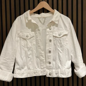 Vit jeansjacka - Snygg vit jeansjacka med knappar framtill och två bröstfickor. Jackan har en klassisk krage och är perfekt för vår och sommar. Den har en croppad passform som ger en trendig look.
