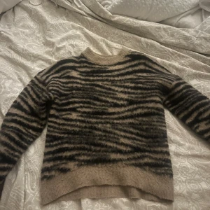 Beige och svart tröja från NA-KD - Säljer en snygg beige och svart tröja från NA-KD med zebramönster. Tröjan är stickad och har långa ärmar, perfekt för kyligare dagar. Den är i storlek XXS och passar dig som gillar en trendig look.