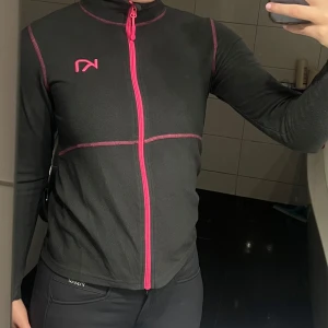 Grå fleecetröjan från Kari Traa - Säljer en svart fleecejacka från Kari Traa med rosa dragkedja och detaljer. Perfekt för kyliga dagar med sin mjuka och varma känsla. Fleecetröjan har en normal passform och långa ärmar. Passar bra som fleecetröja i stallet eller som ett extra lager! 
