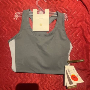 Grå linnetopp från athlecia ( ny pris 449kr) - Snygg och sportig grå linnetopp från Lululemon med vita sidopaneler. Perfekt för träning med sin bekväma passform och stilrena design. Ny med taggar kvar.