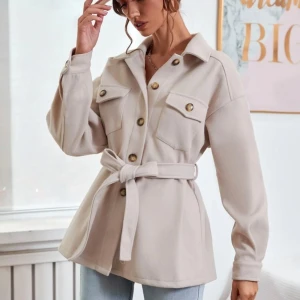 Beige overshirt med bälte - Snygg beige overshirt med knappar och bälte i midjan. Jackan har långa ärmar och två bröstfickor med lock. Perfekt för en stilren look.